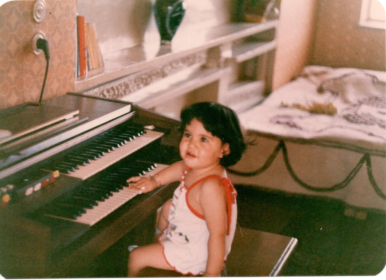 A baby sits in front of a piano.