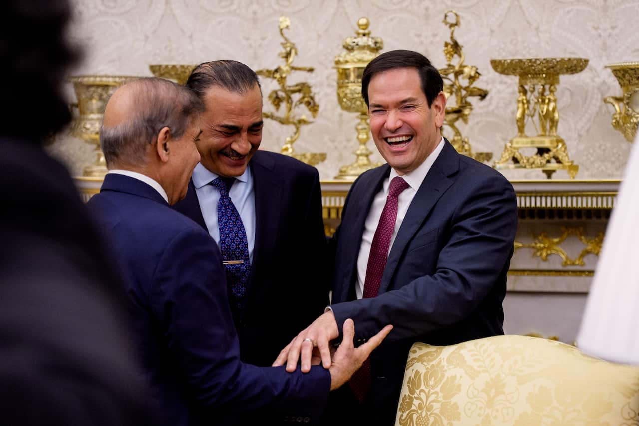 US Secretary of State Marco Rubio laughs while reaching out to shake hands with Pakistani Prime Minister Shehbaz Sharif and Pakistani General Asim Munir in a formal room decorated with ornate gold trophies.