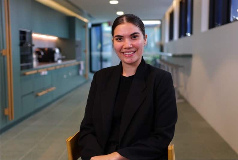 A young woman sitting down and smiling at a camera