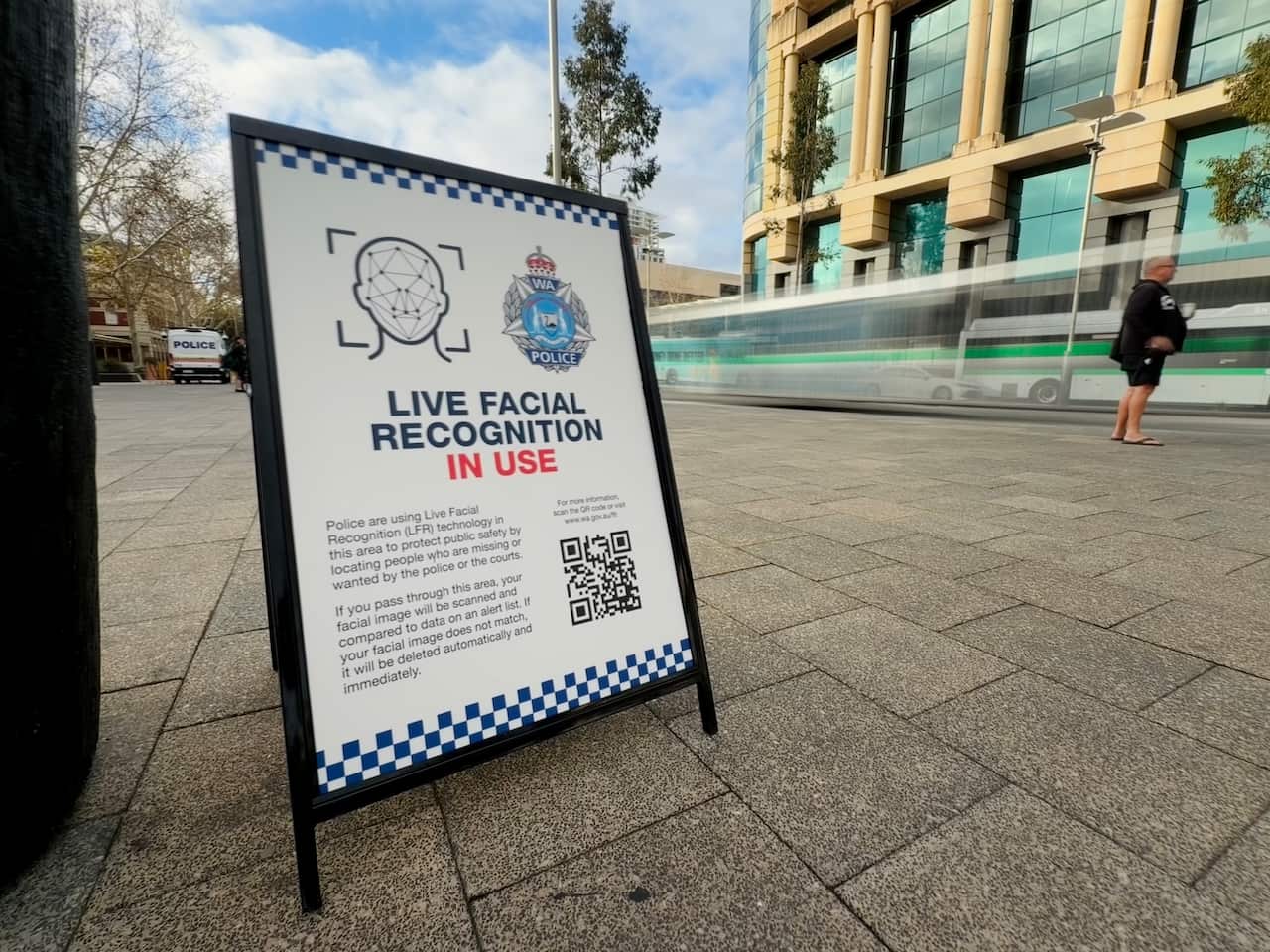 A police billboard on an urban pavement indicating facial recognition is being used in the area.