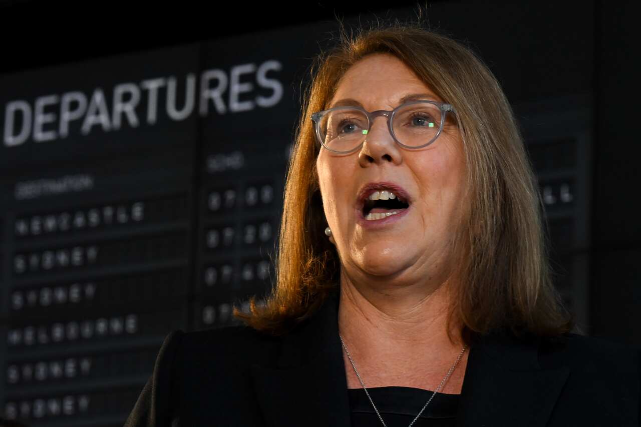 Catherine King speaking in front of an airport departures board.