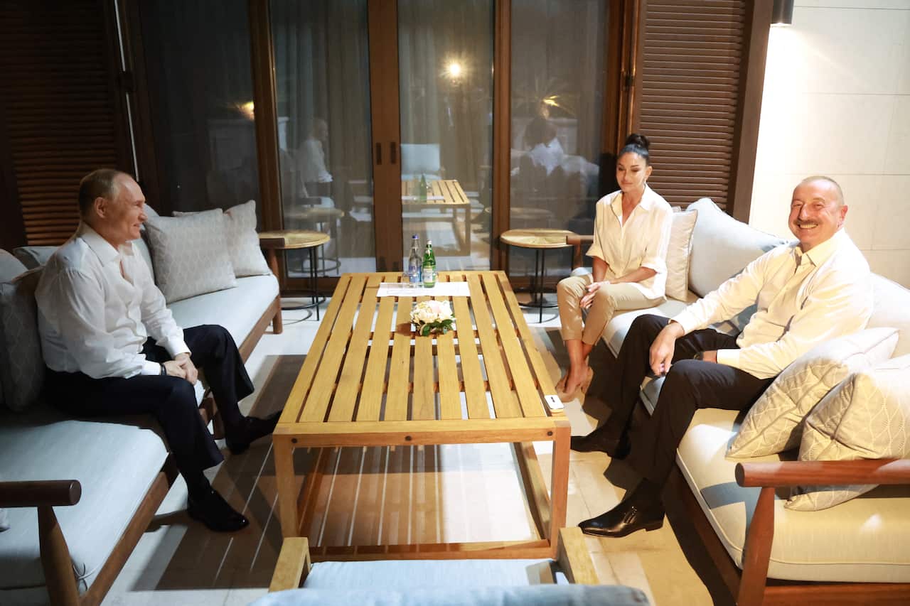 Three people sit smiling around a table inside.
