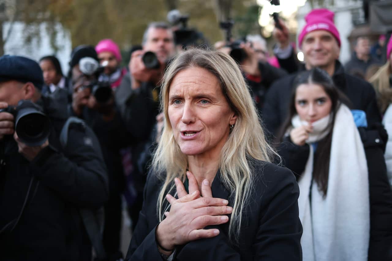 A blonde woman speaking while surrounded by supporters.