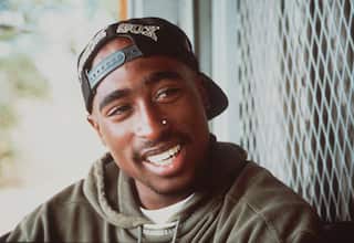 A young man wearing a cap backwards is smiling as he looks sideways.
