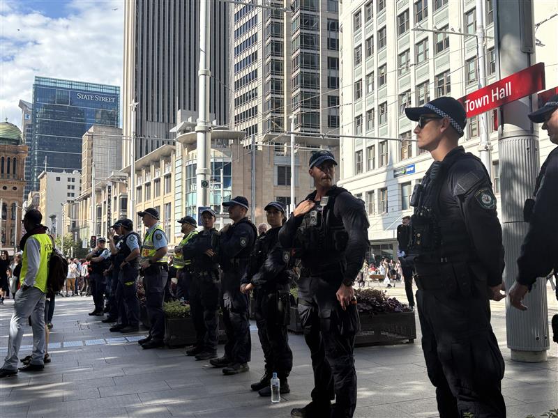 A row of police officers standing in front of a light rail sign for Town Hall.