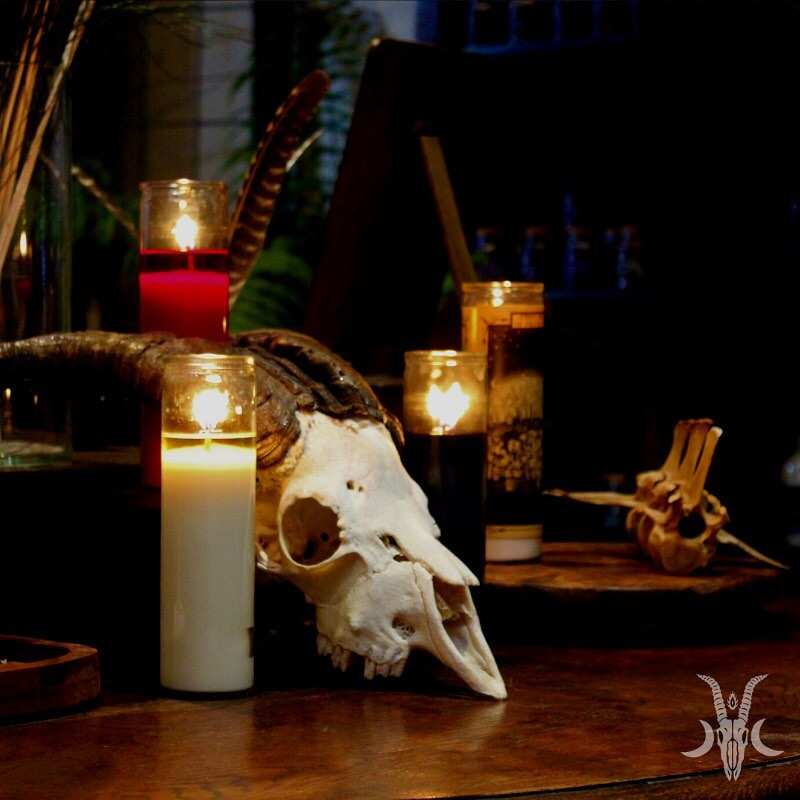 A steer skull with long horns sits amongst burning candles on a wooden table