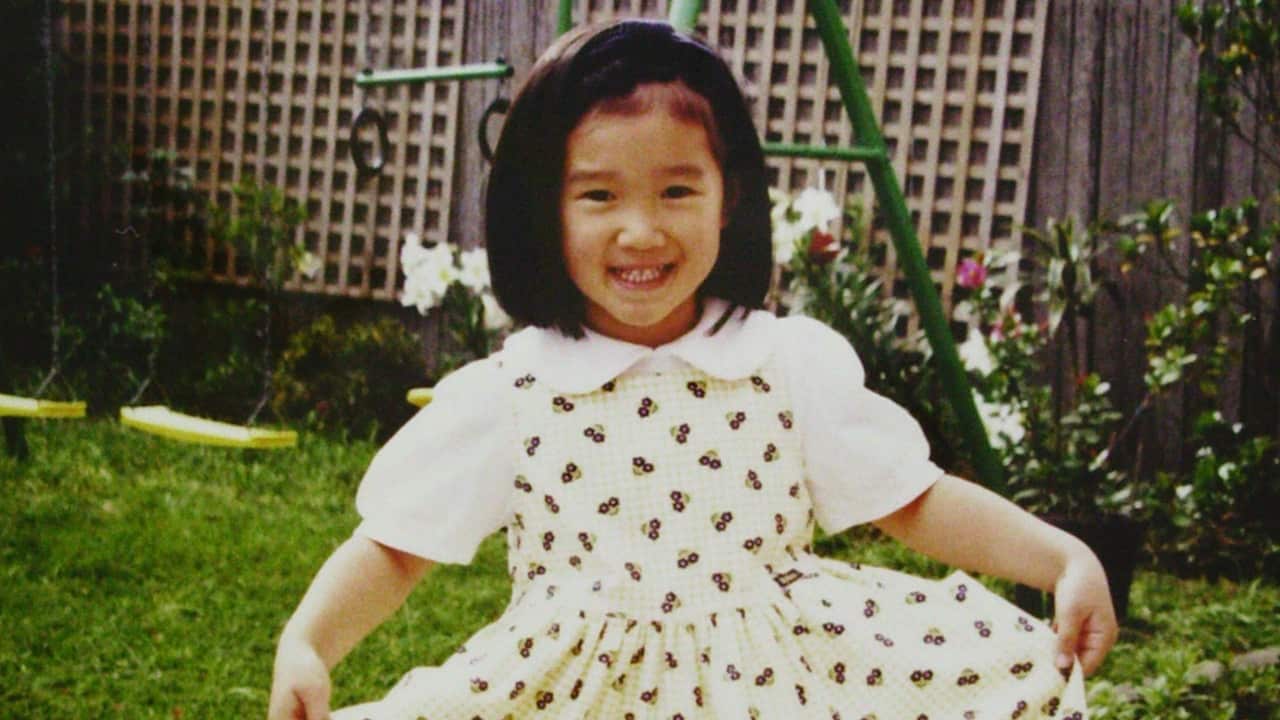 a vintage photo of a young girl with a black bob in a white dress in the backyard with a swingset