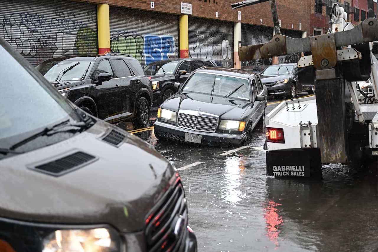 Cars driving along a street that is partially flooded.