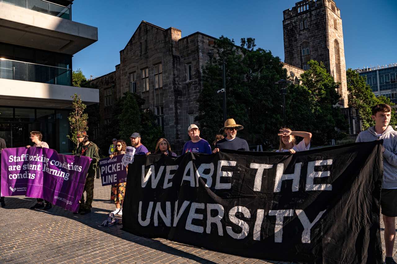 Union members protest standing behind a banner which says "We Are The University".