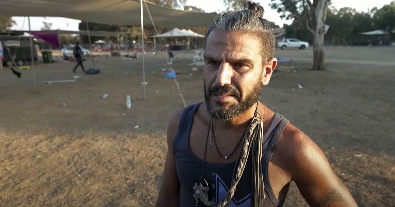 The organiser of the Supernova rave stands in the abandoned festival site wearing a singlet and necklaces.