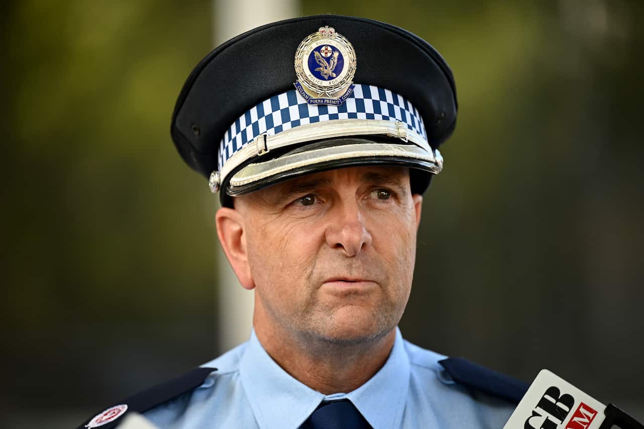 A police officer in uniform speaking into media microphones.