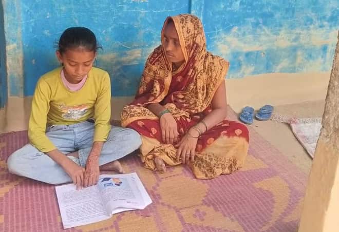 A photo of a young Nepalese girl sitting beside her mother, while reading a book.