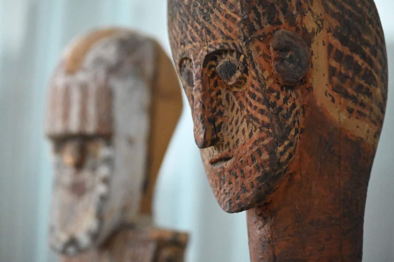 A carved face and neck, with detailed ears, nose eyes and mouth, painted in the Tiwi cross-hatching style.