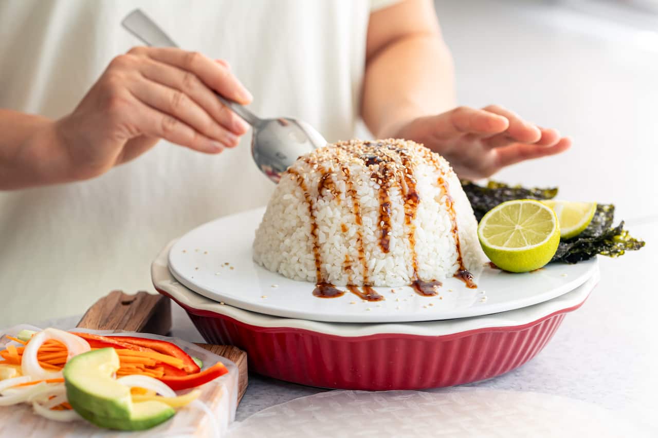 A woman prepares spring rolls with rice and vegetables.