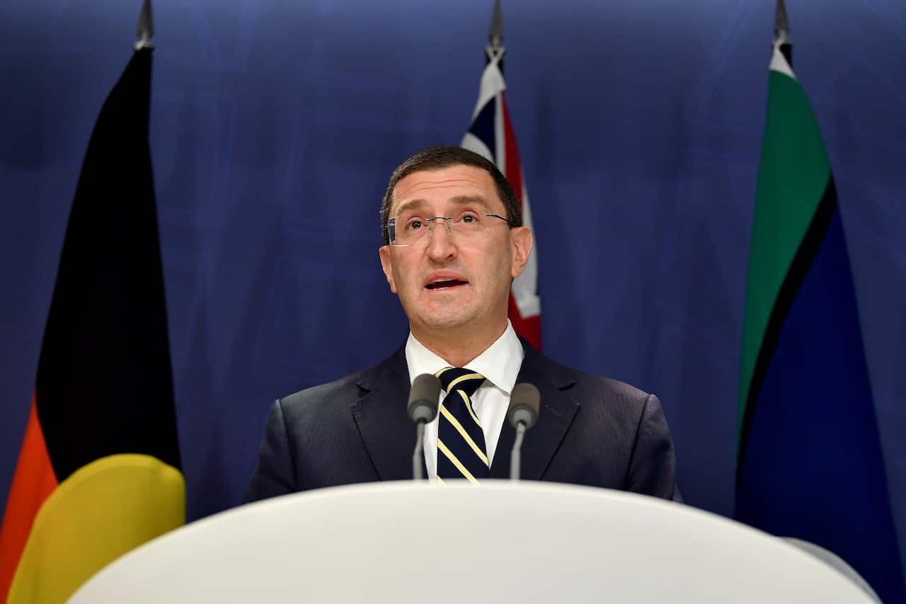 Man in suit stands at lectern in front of Indigenous flags.