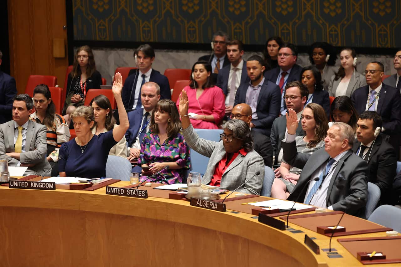 A group of people seated around a circular table. Some of them have their hands raised.