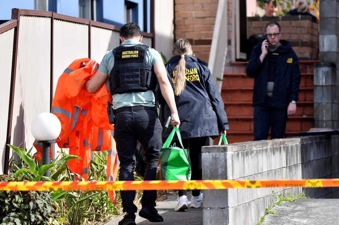 Three Border Force officers in blue uniforms outside a home