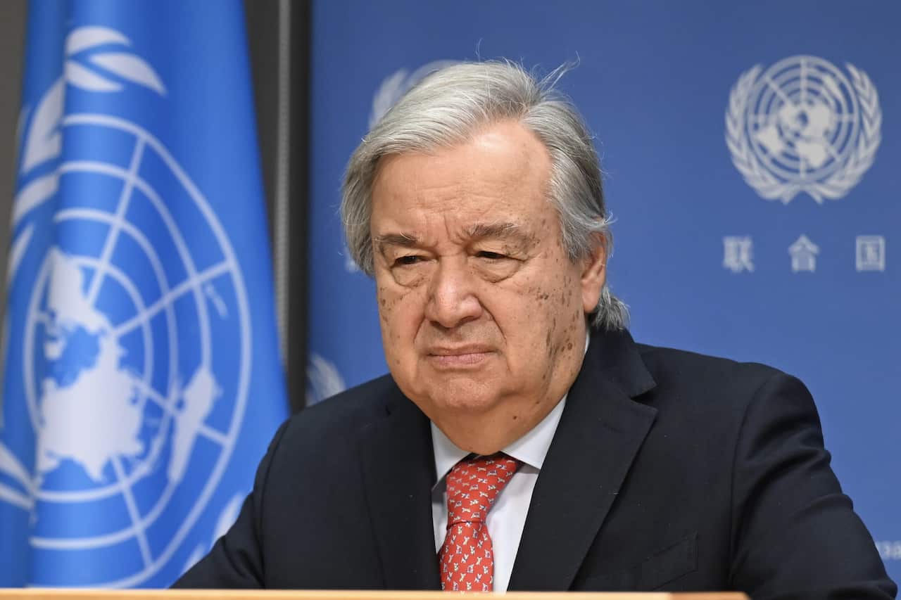 Antonio Guterres wearing a suit in front of the United Nations flag
