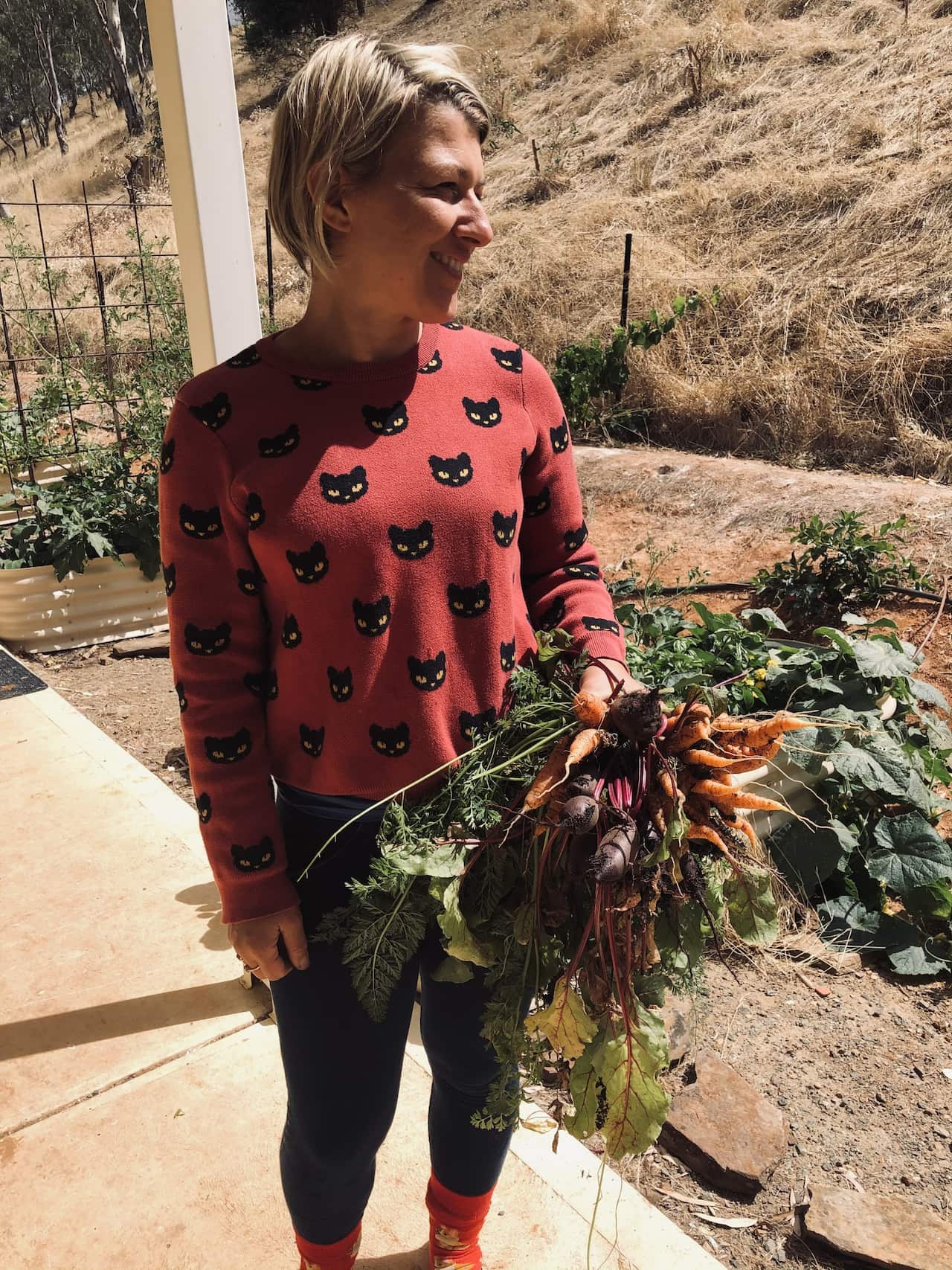 A woman standing outside holding a bunch of carrots.