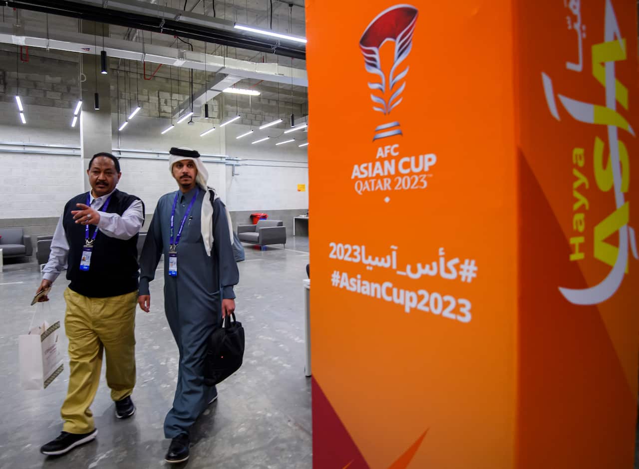 Two people walk past a large orange Asian Football Cup sign. 