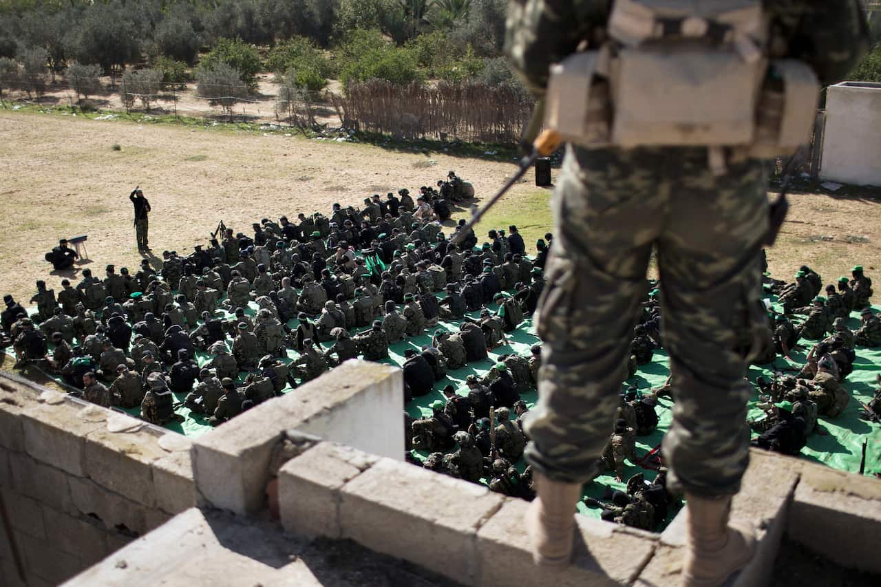 A soldier standing on a wall looks down upon a large group of people sitting.