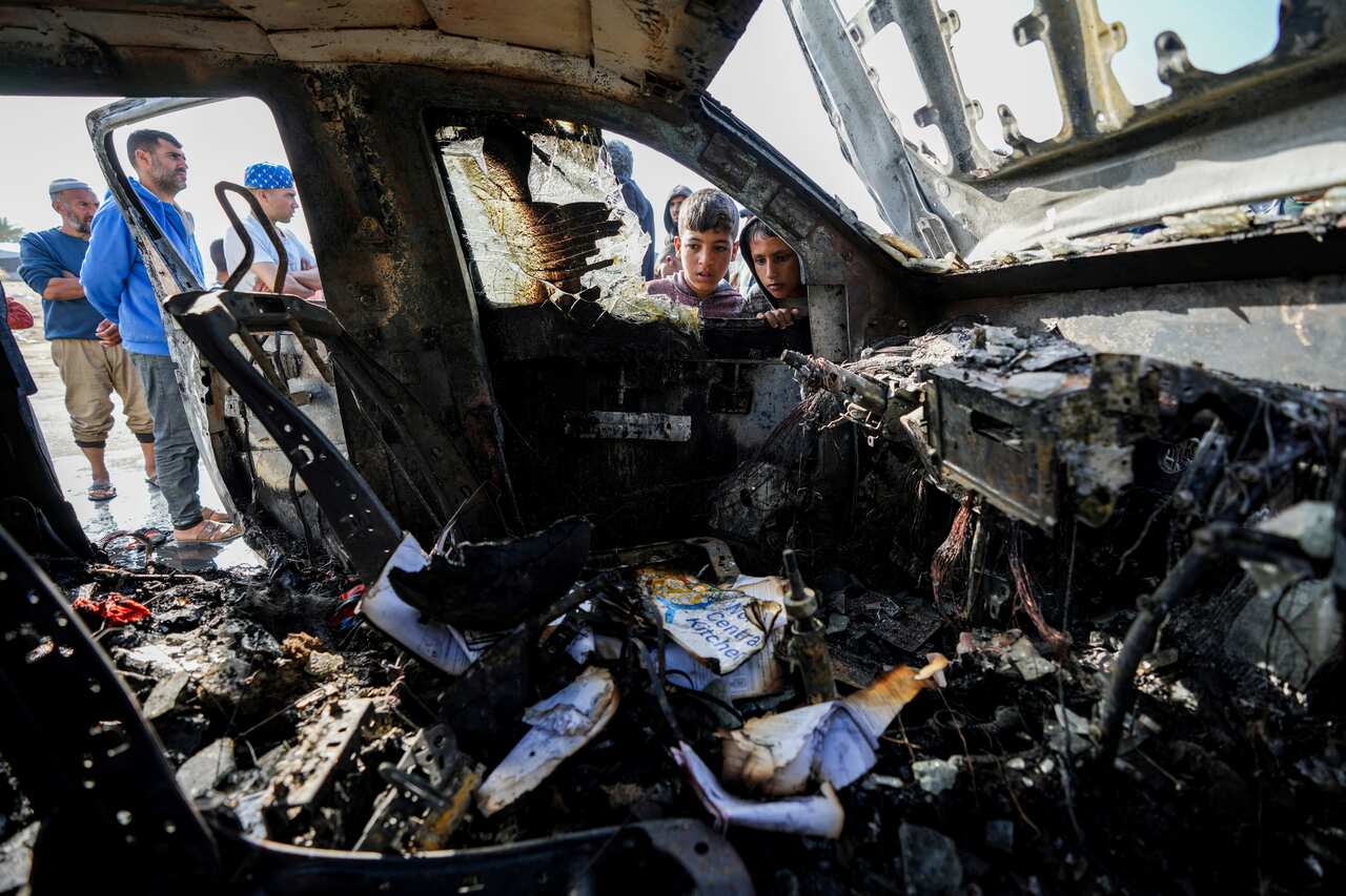 People inspect a burnt-out car