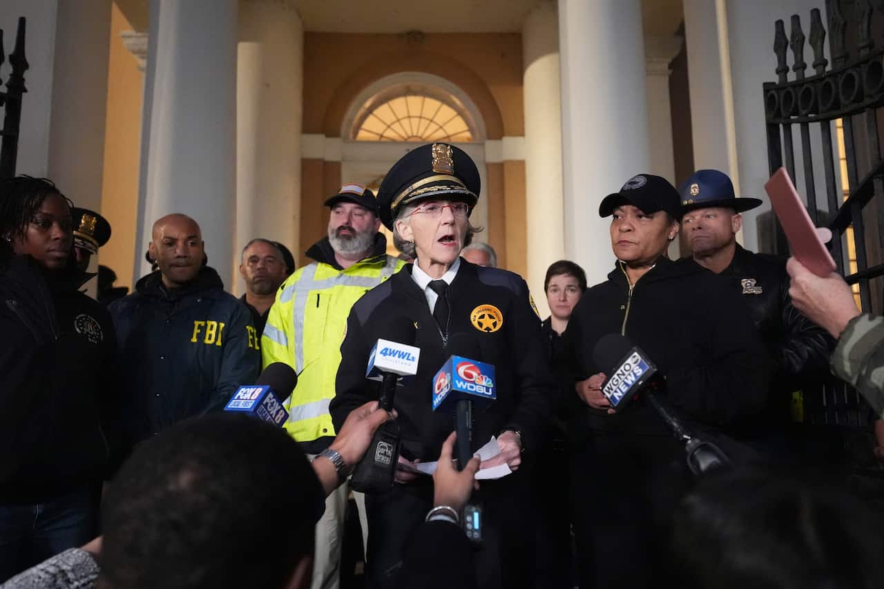 A police officer speaks at a press conference surrounded by other officials and journalists.