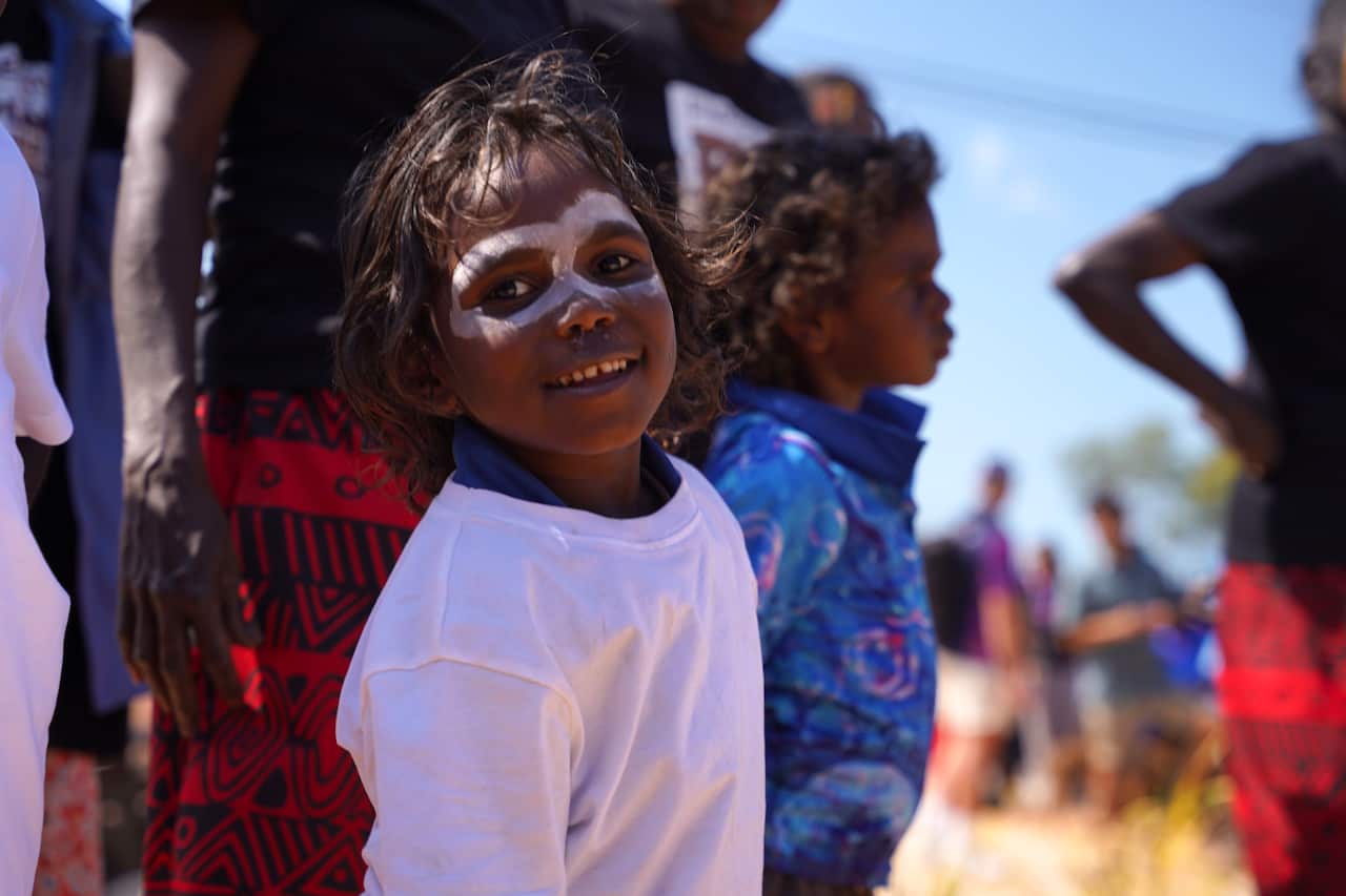 A child with white face paint smiling and looking at the camera