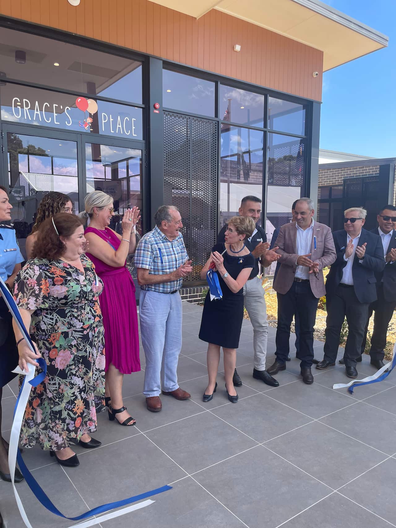 A woman cuts a ribbon to signal the opening of a building. A line of people stand next to her.