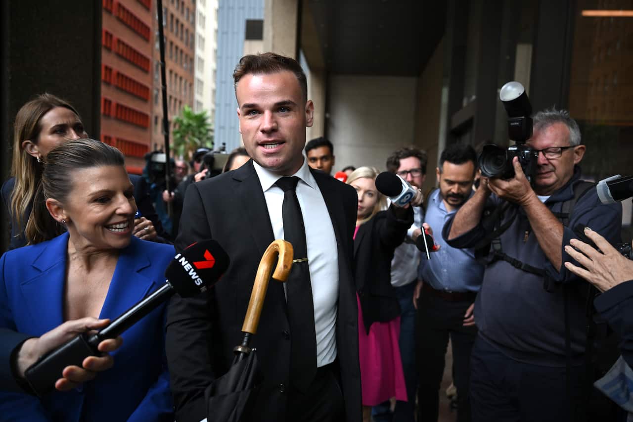 A man in a suit walking through a crowd of people outside court