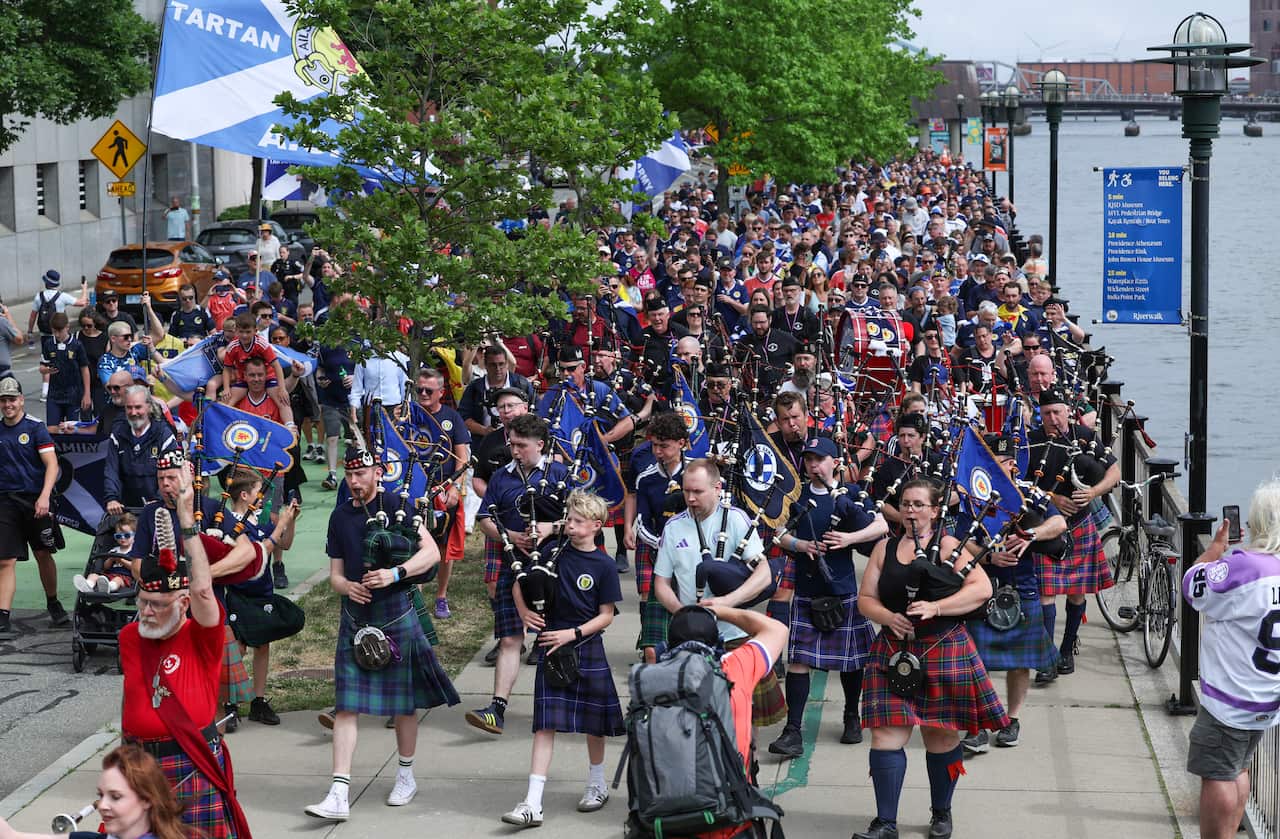 Scottish football fans, known as the Tartan Army, many wearing kilts and carrying bagpipes, marching on a street