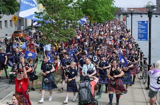 Scottish football fans, known as the Tartan Army, many wearing kilts and carrying bagpipes, marching on a street
