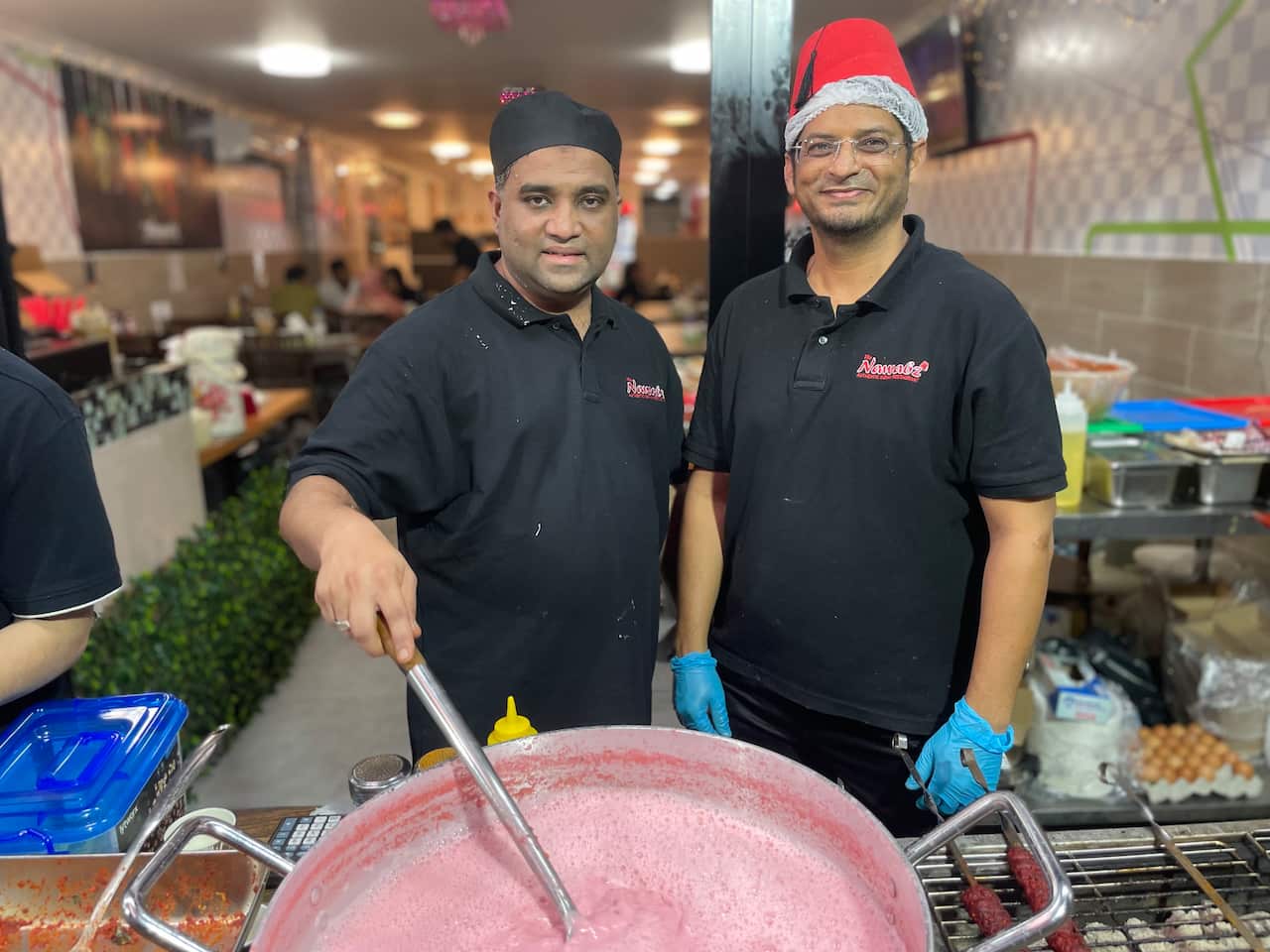 Men stand in front of a big pot of pink tea. 