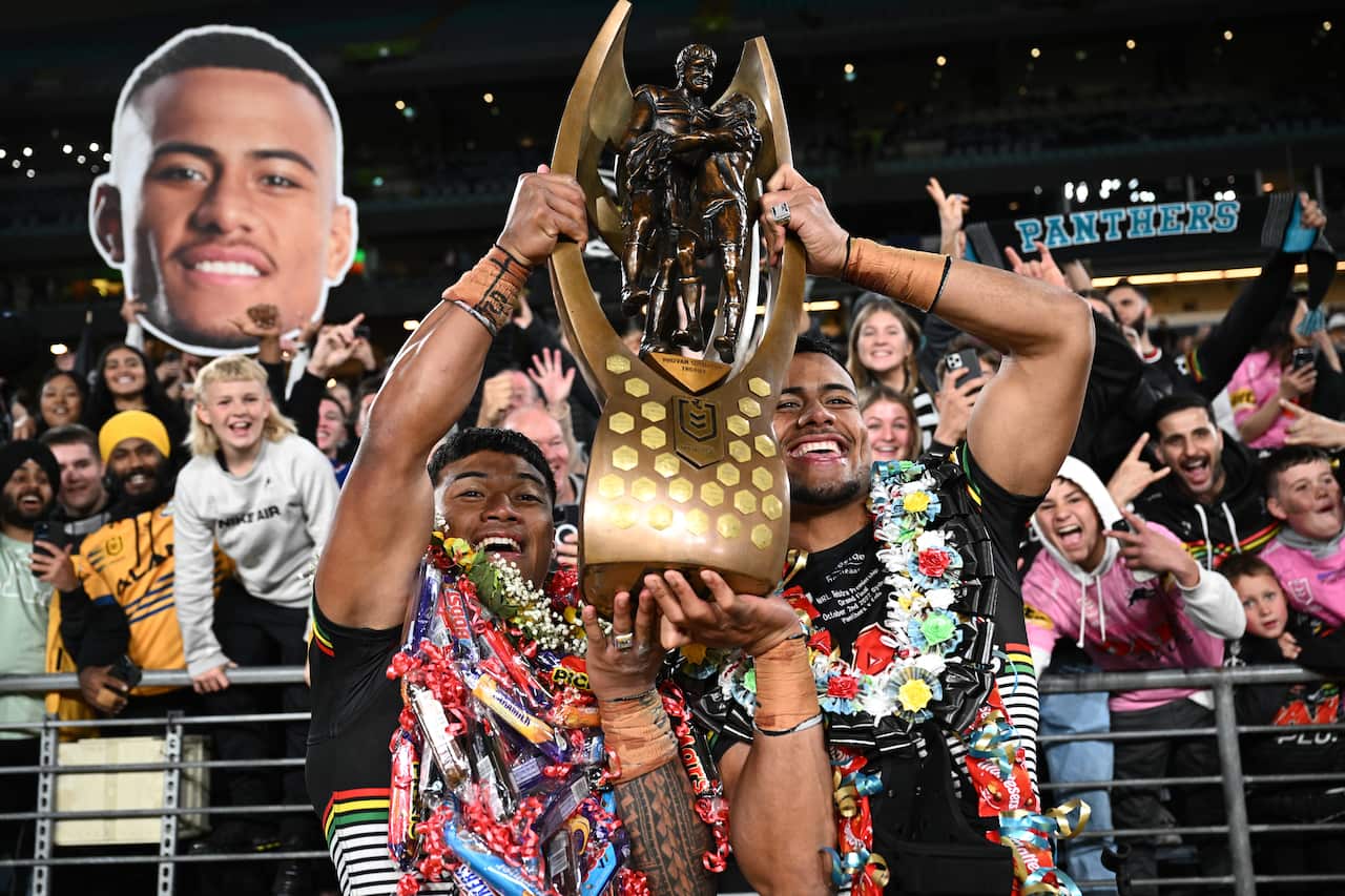 Two men carry a trophy while wearing colourful leis. 