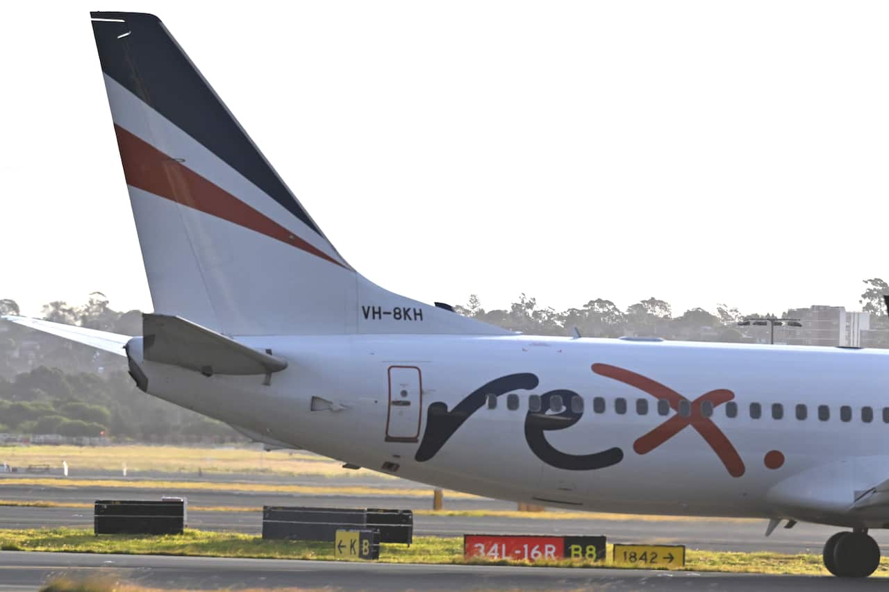 A plane on a runway. The word rex is painted on the side of the plane.