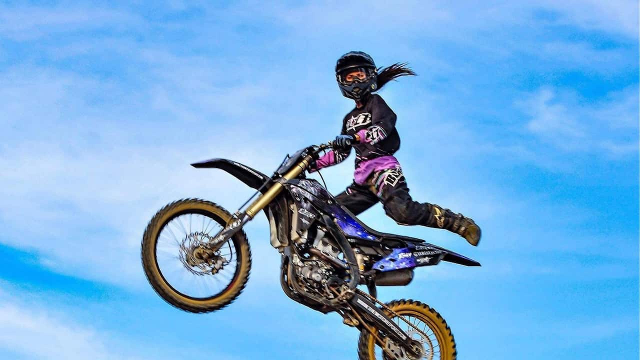 a woman on a motorcycle does a jump trick in the air