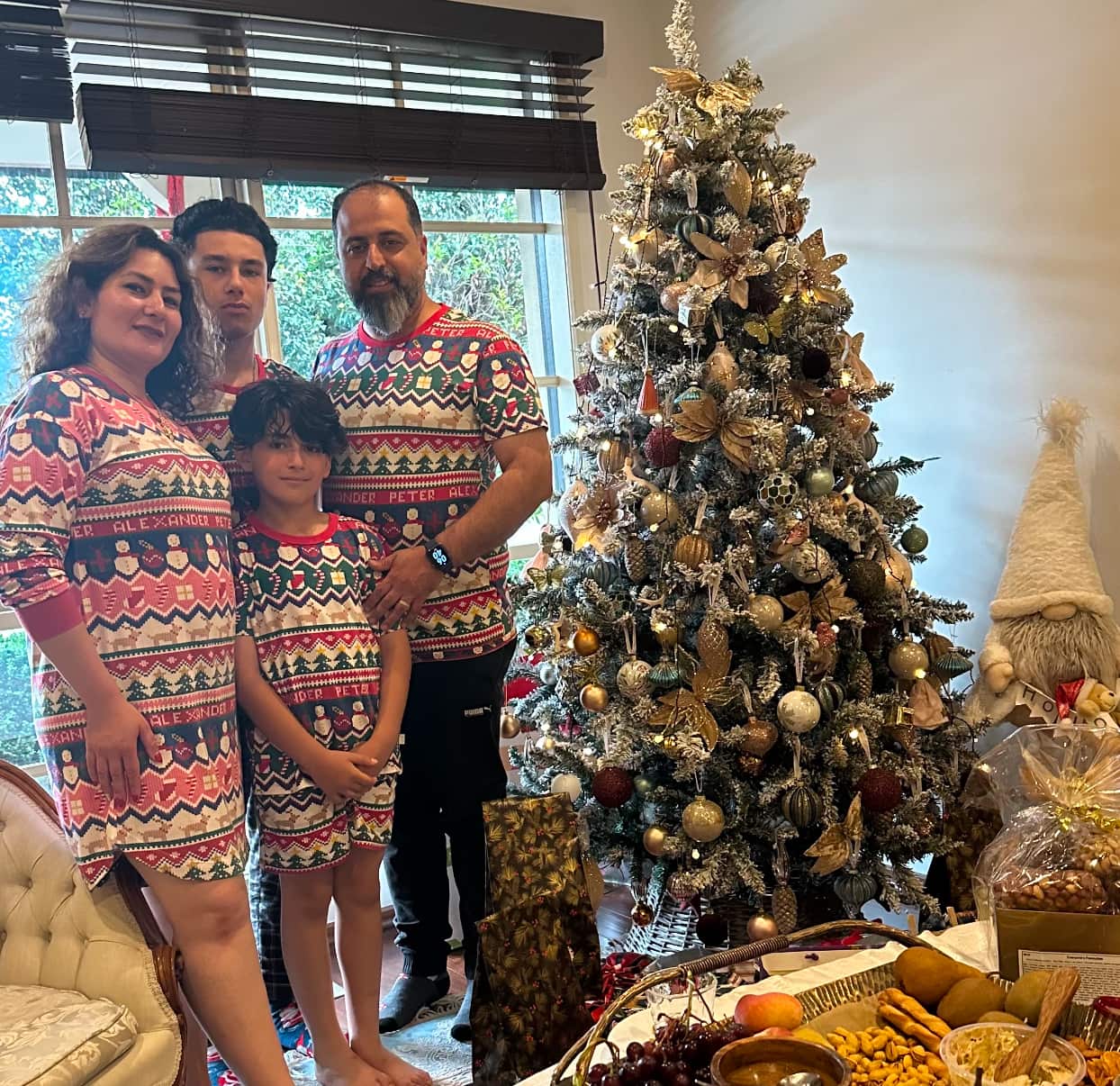 A mother, father and two sons stand next to a Christmas tree wearing matching Christmas outfits.