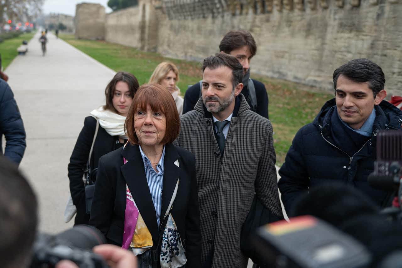 A woman standing in front of cameras on a footpath, flanked by three men and two women.
