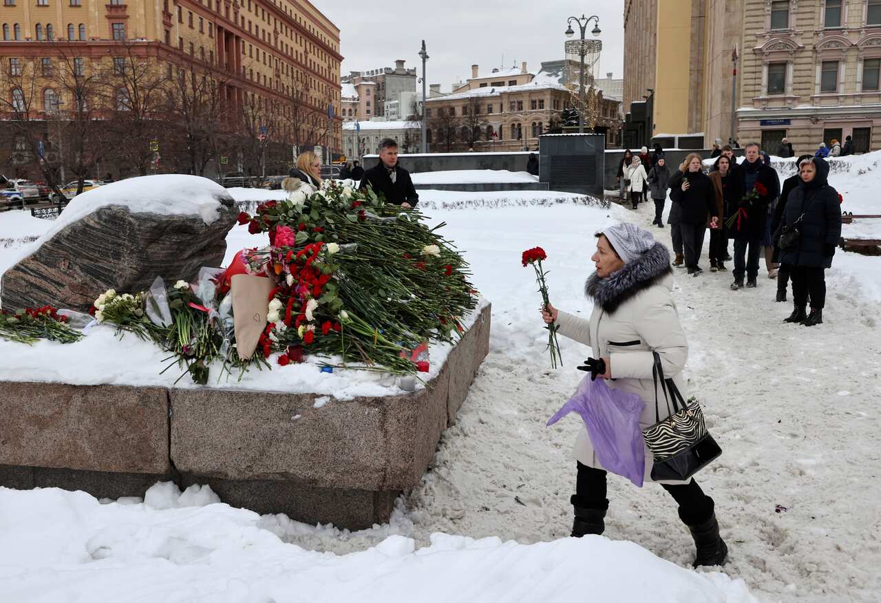 A woman carrying a rose walks towards a plinth where other roses have been laid.