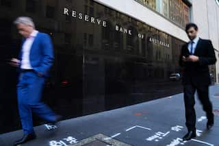 Two men in suits looking at their phones walk past the outside of the Reserve Bank in Sydney