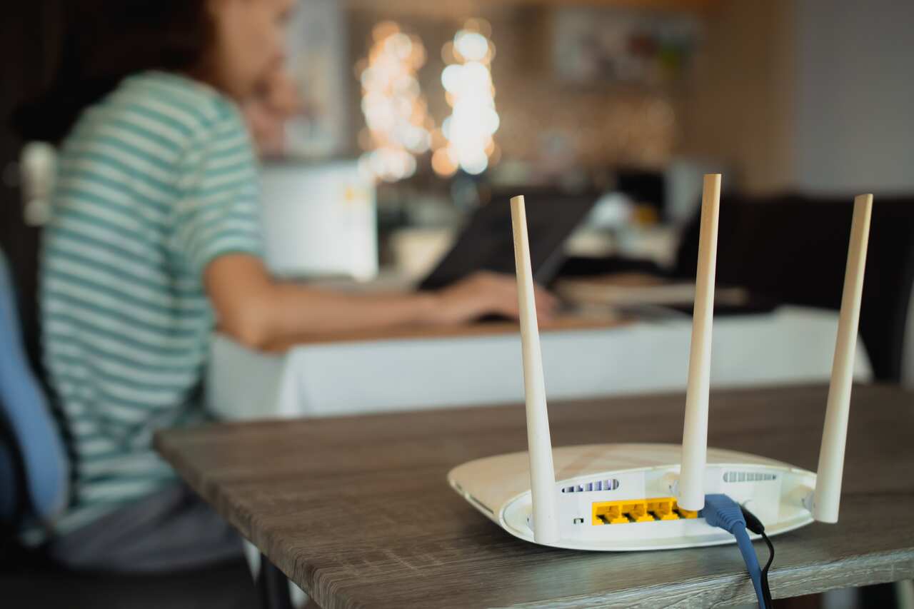 A woman sits in a blurred background that has a modem in front.