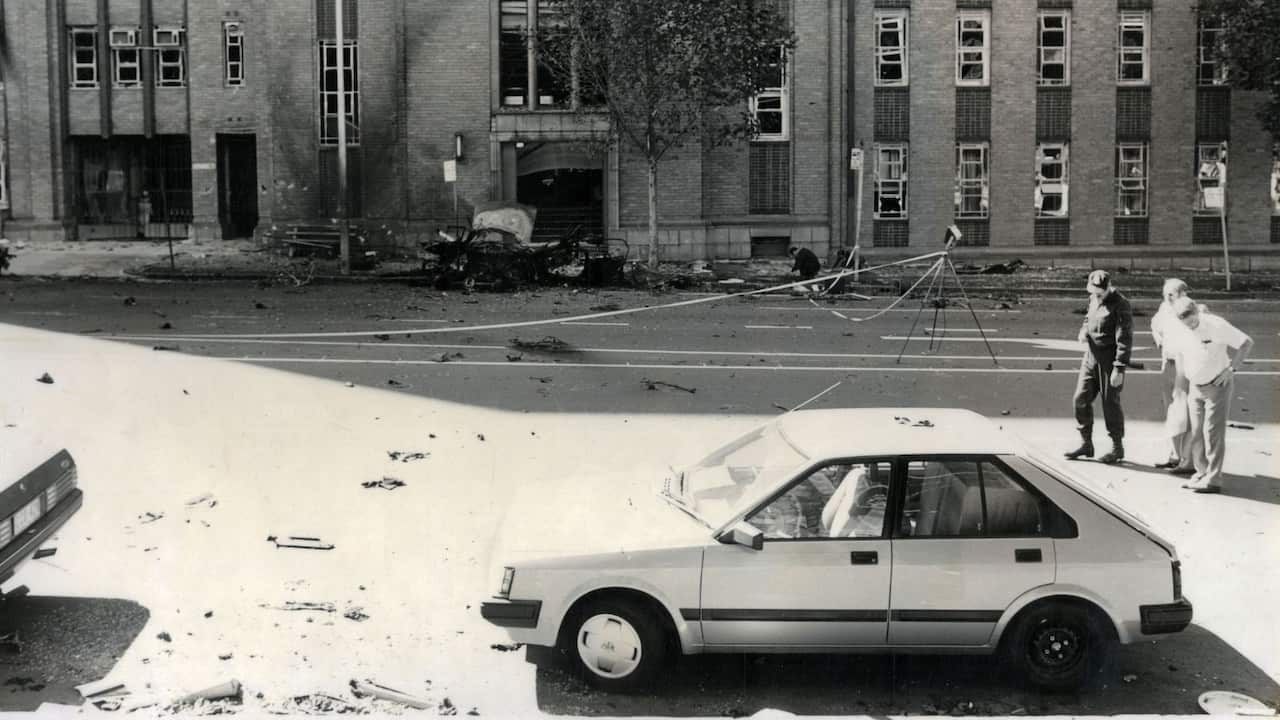 a black and white photo of car debris on the road following an explosion in front of a police station