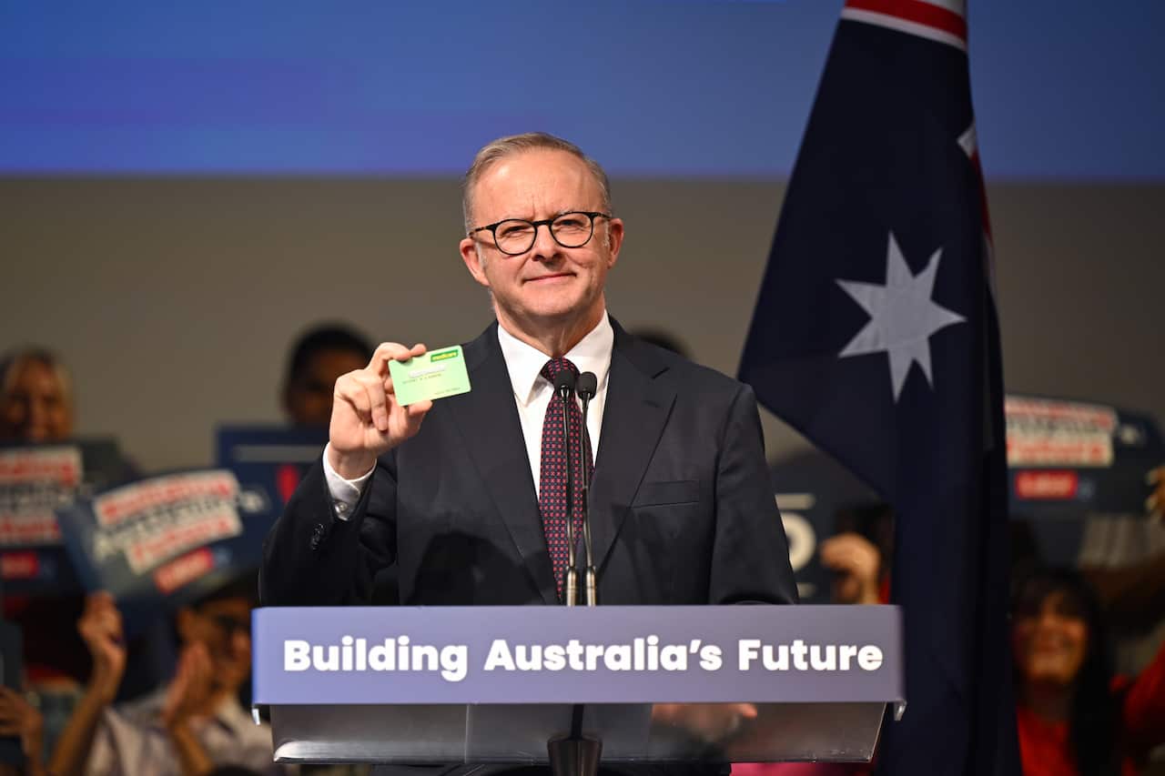 Anthony Albanese holds up a green Medicare card as he stands in front of the Australian flag during a rally.