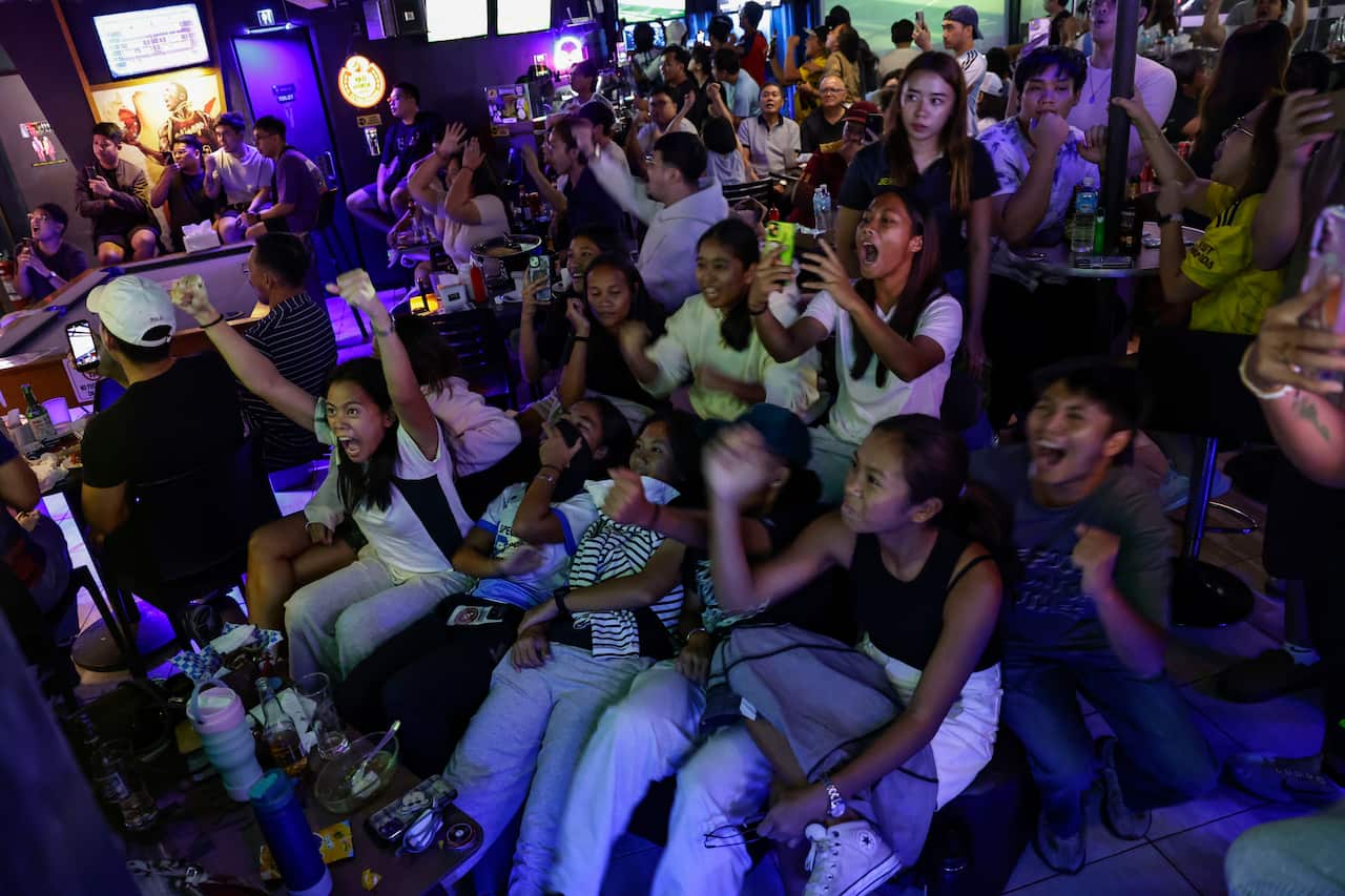 A large group of people in a bar watching a TV.