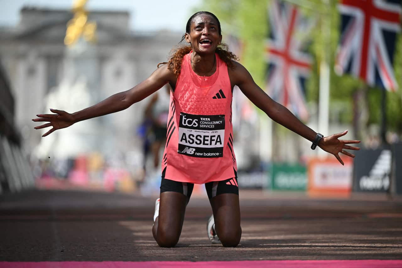 A woman marathon runner celebrates after winning a race, she is on her knees and her arms are wide open