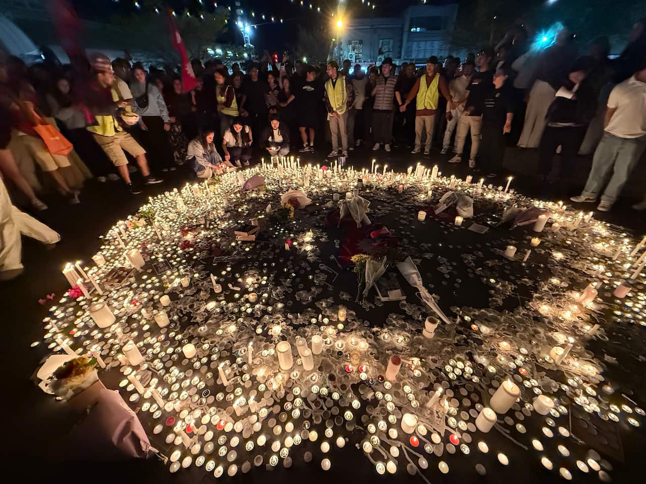 People stand around a large circle of candles at a night-time vigil. 