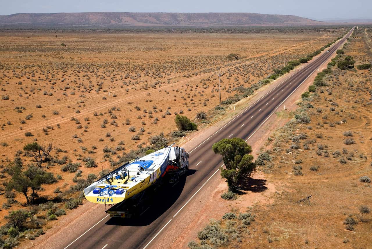 Truck with a yacht on it drives through the desert.