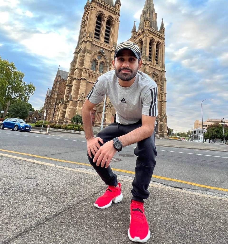 A man kneels down to smile ina photo behind a heritage building. 
