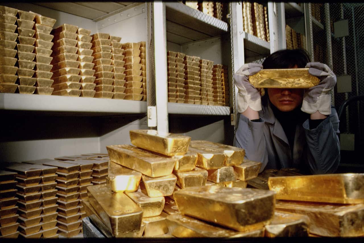 A person surrounded by stacks of gold bars