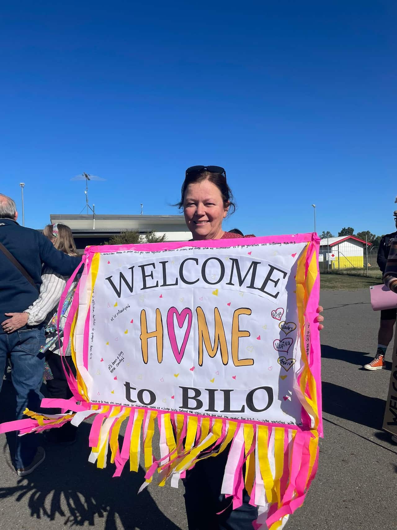 Woman holding sign which reads 'welcome home to Bilo'